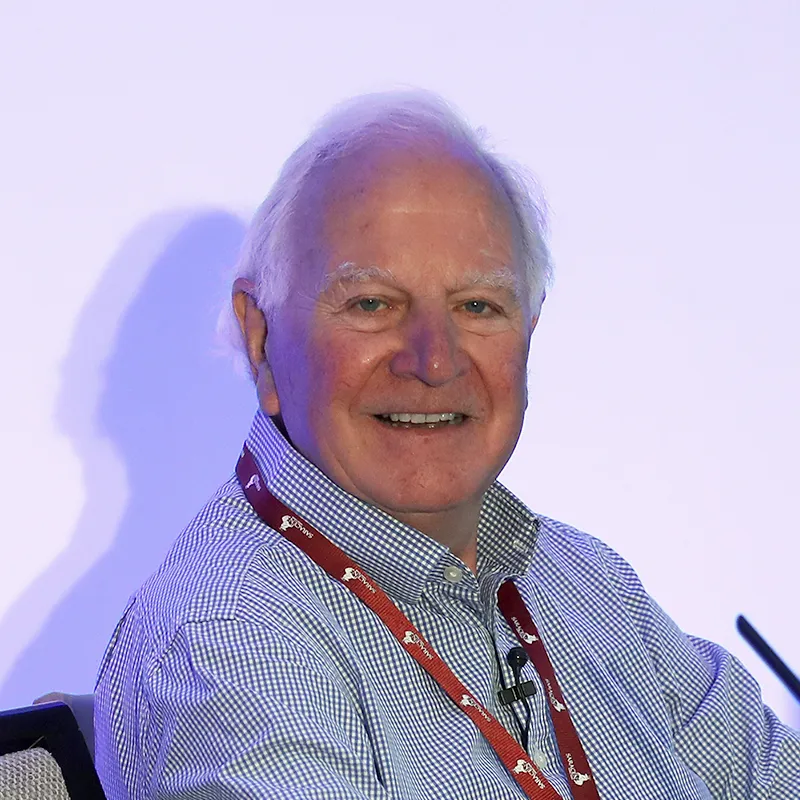 Smiling elderly man with white hair wearing a checkered shirt and red lanyard.