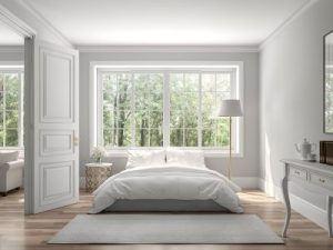 Beautiful all white bedroom with white carpet and white bed and a large white window in the background looking out at trees