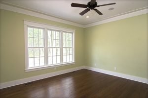 White windows letting light into a green room with a ceiling fan