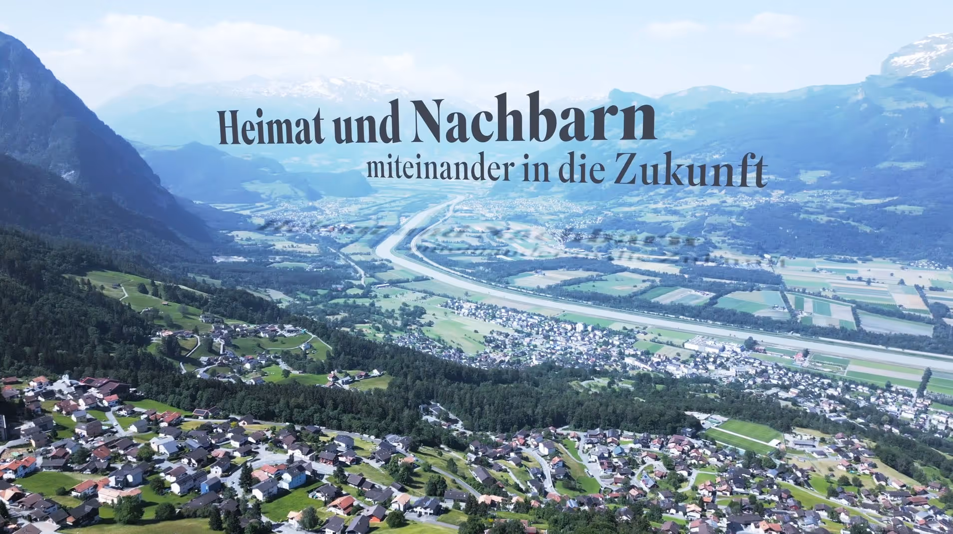 Luftaufnahme des Rheintals mit Dörfern, Feldern, einer Autobahn und Bergen, Text: „Heimat und Nachbarn miteinander in die Zukunft“. Links ist das Fürstentum Liechtenstein, rechts vom Rhein die Schweiz.