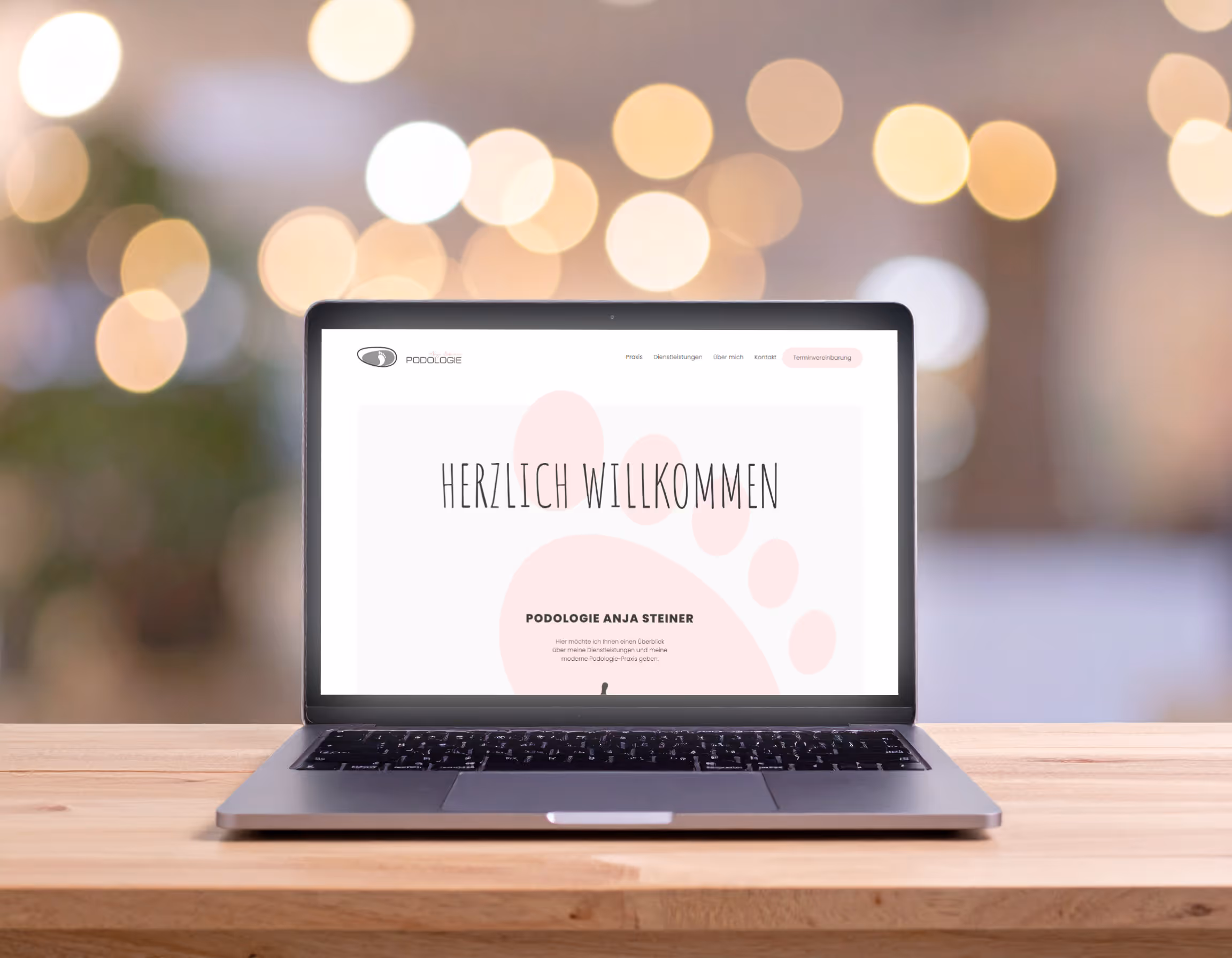 Laptop auf Holztisch mit der Webseite "Podologie Anja Steiner" und dem Willkommenstext "HERZLICH WILLKOMMEN".