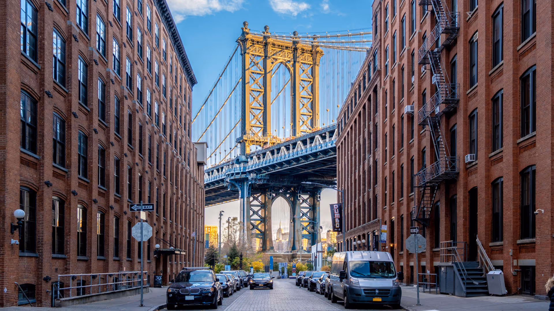 Foto vum Hutter. Die Manhattan Bridge rahmt eine Strasse zwischen hohen Backsteingebäuden in DUMBO, Brooklyn, New York, ein.