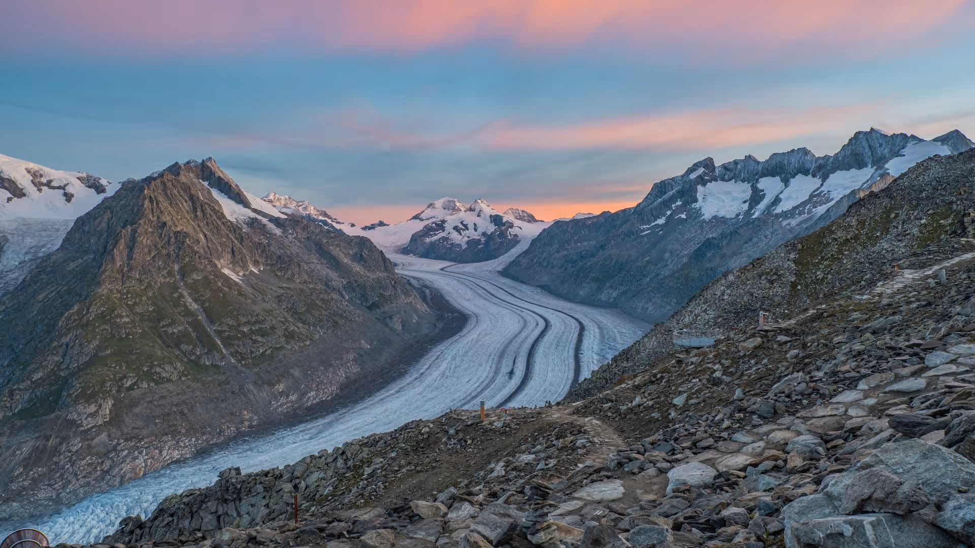 Dämmerungsblick auf den Grossen Aletschgletscher, umrahmt von Fels- und Schneegipfeln, mit rosa-blauem Himmel.