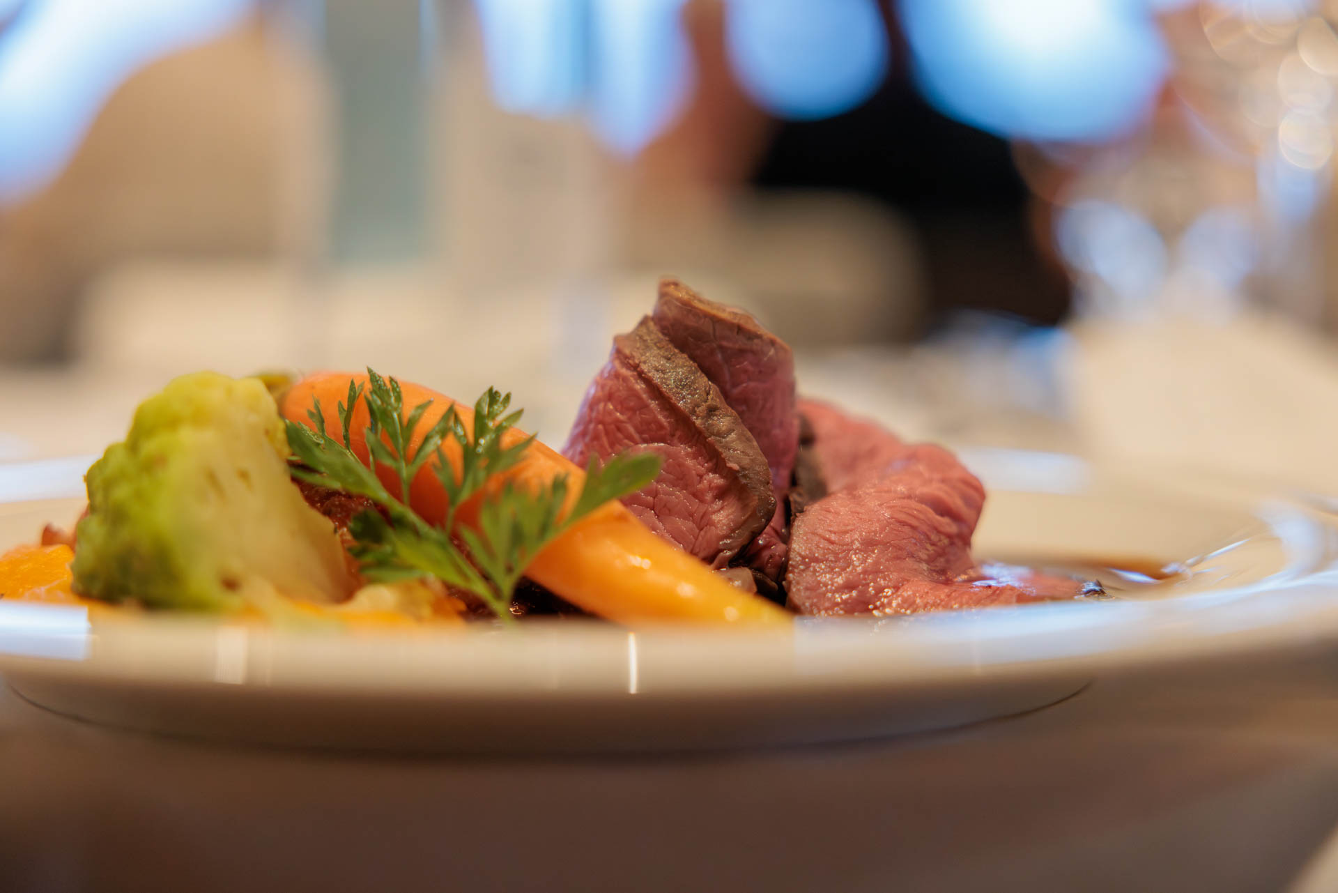 Angerichteter Hauptgang mit rosa gebratenem Rindfleisch, Karotten und Romanesco auf weissem Teller