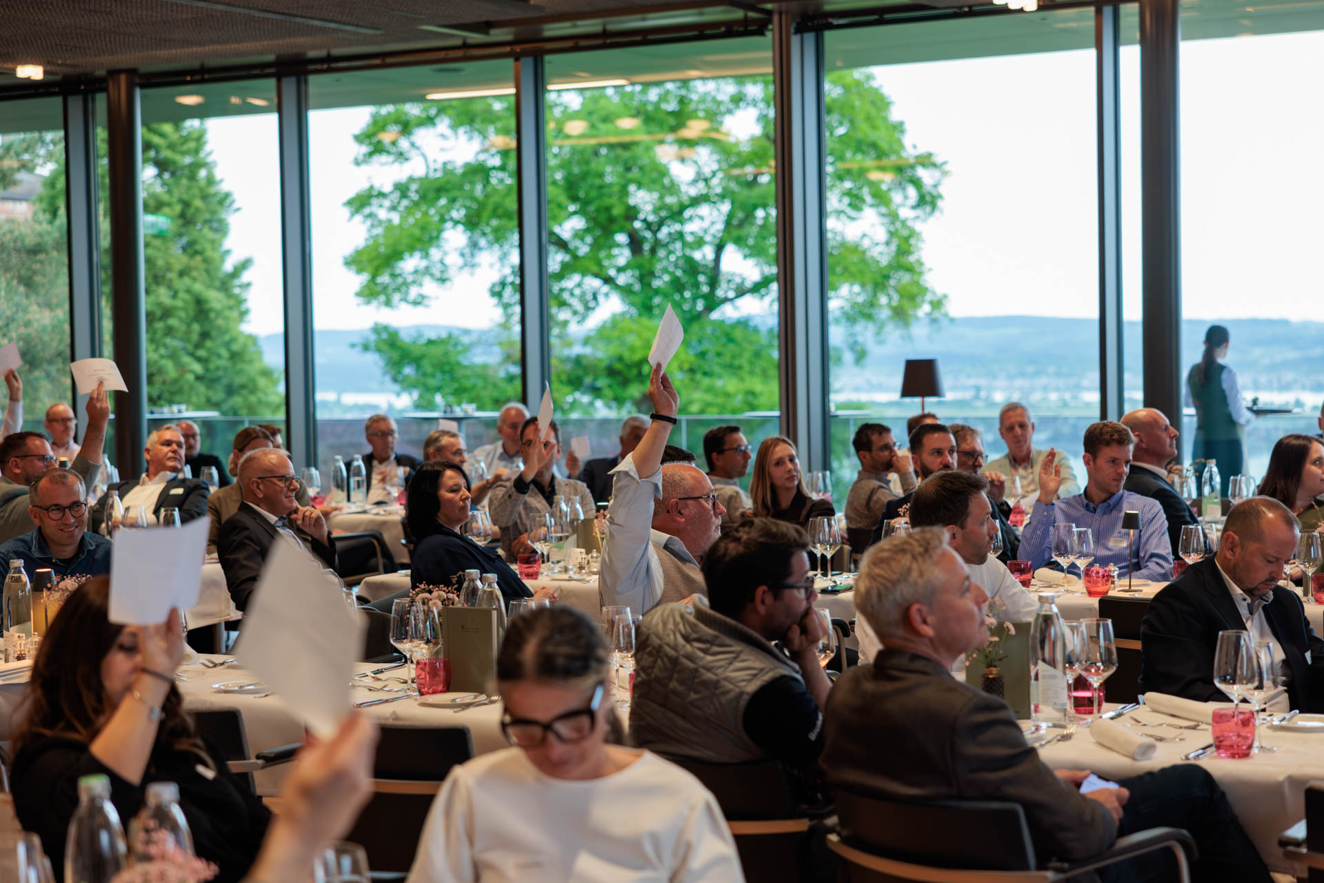 Mitglieder stimmen mit erhobenen Stimmkarten ab, im Hintergrund die Fensterfront zum Bodensee