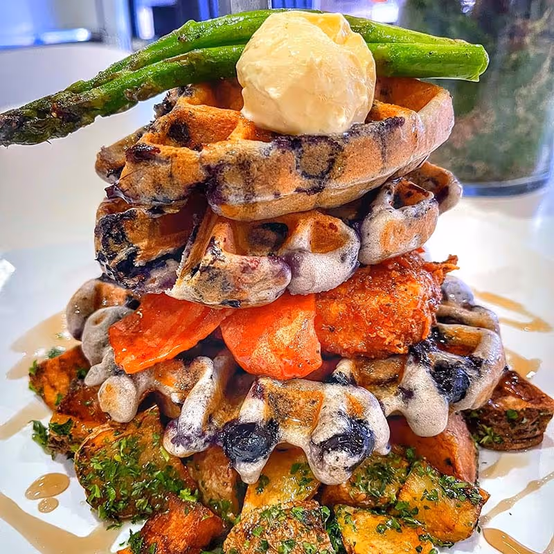 A stack of waffles with butter and vegetables on top.