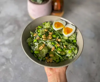 Bol de salade verte aux épinards tenu à la main, garni de deux moitiés d'œuf dur, graines de tournesol et petits pois, sur fond de plan de travail en marbre