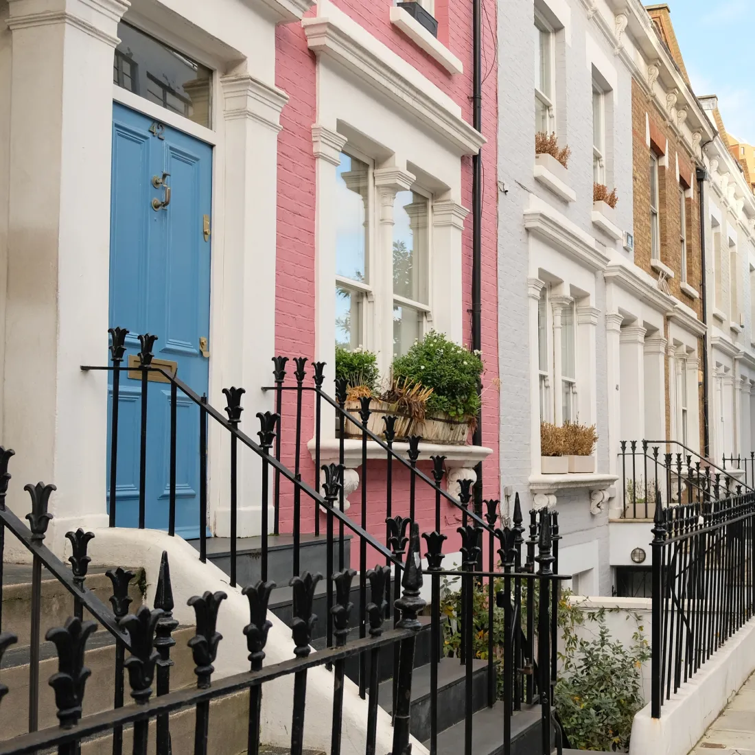 A row of Victorian London houses, painted in pastels, with steps leading up to them.