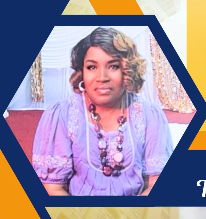 Woman with curly hair wearing a purple dress and a beaded necklace, sitting indoors with decorative curtains in the background.