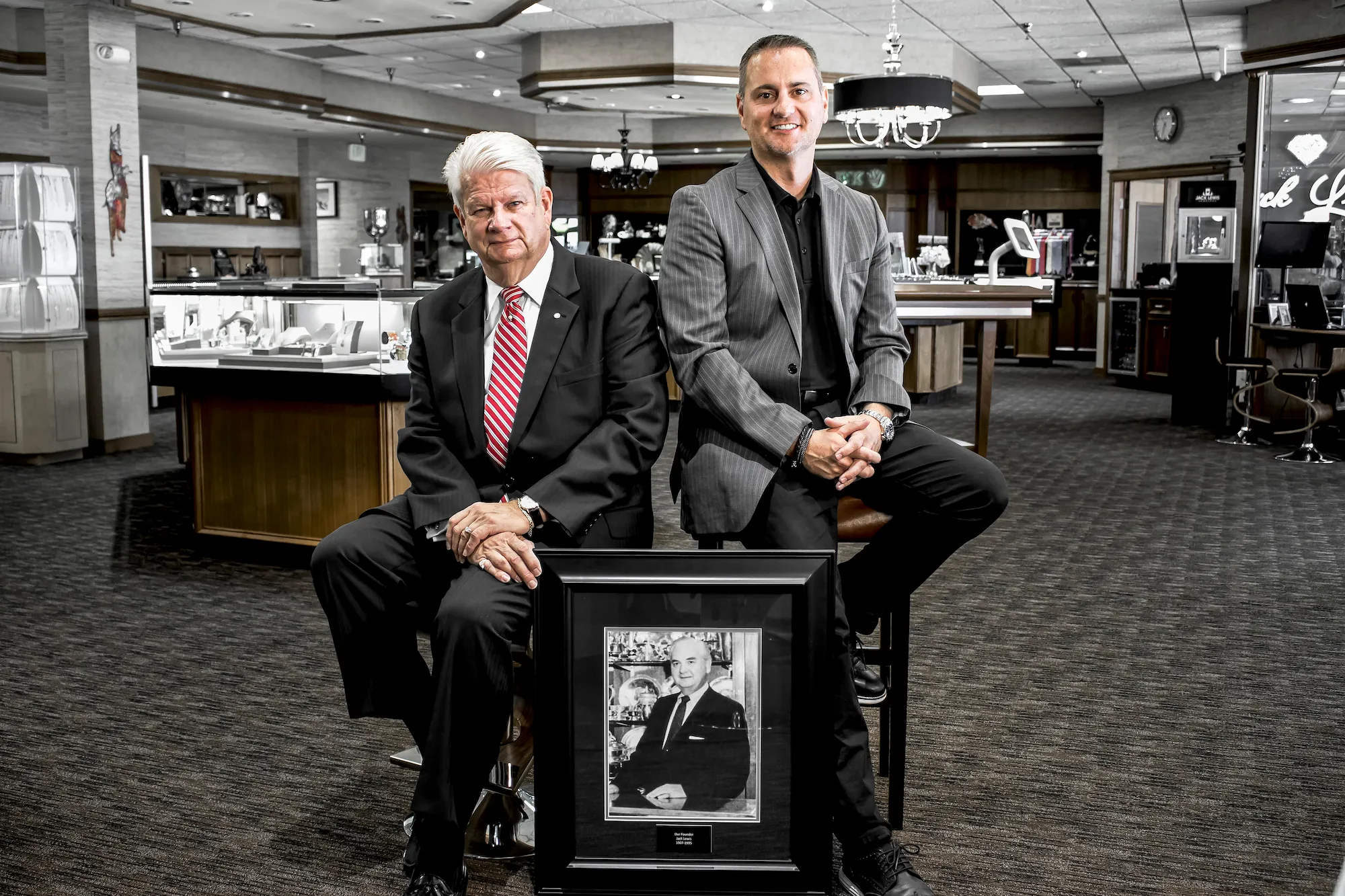 a black and white framed portrait of original owner Jack Lewis is situated behind the 2nd CEO John Wohlwend and the the current CEO John Carter