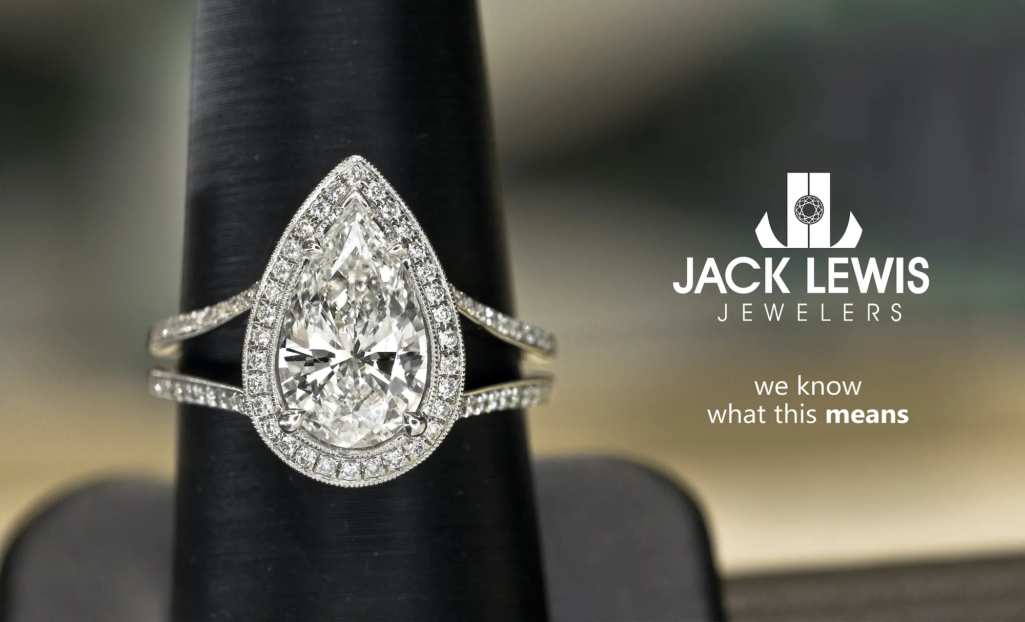 Advertising billboard with a large pear shaped diamond engagement ring set in white gold. It sits next to the Jack Lewis Jewelers logo and has the phrase "we know what this means"