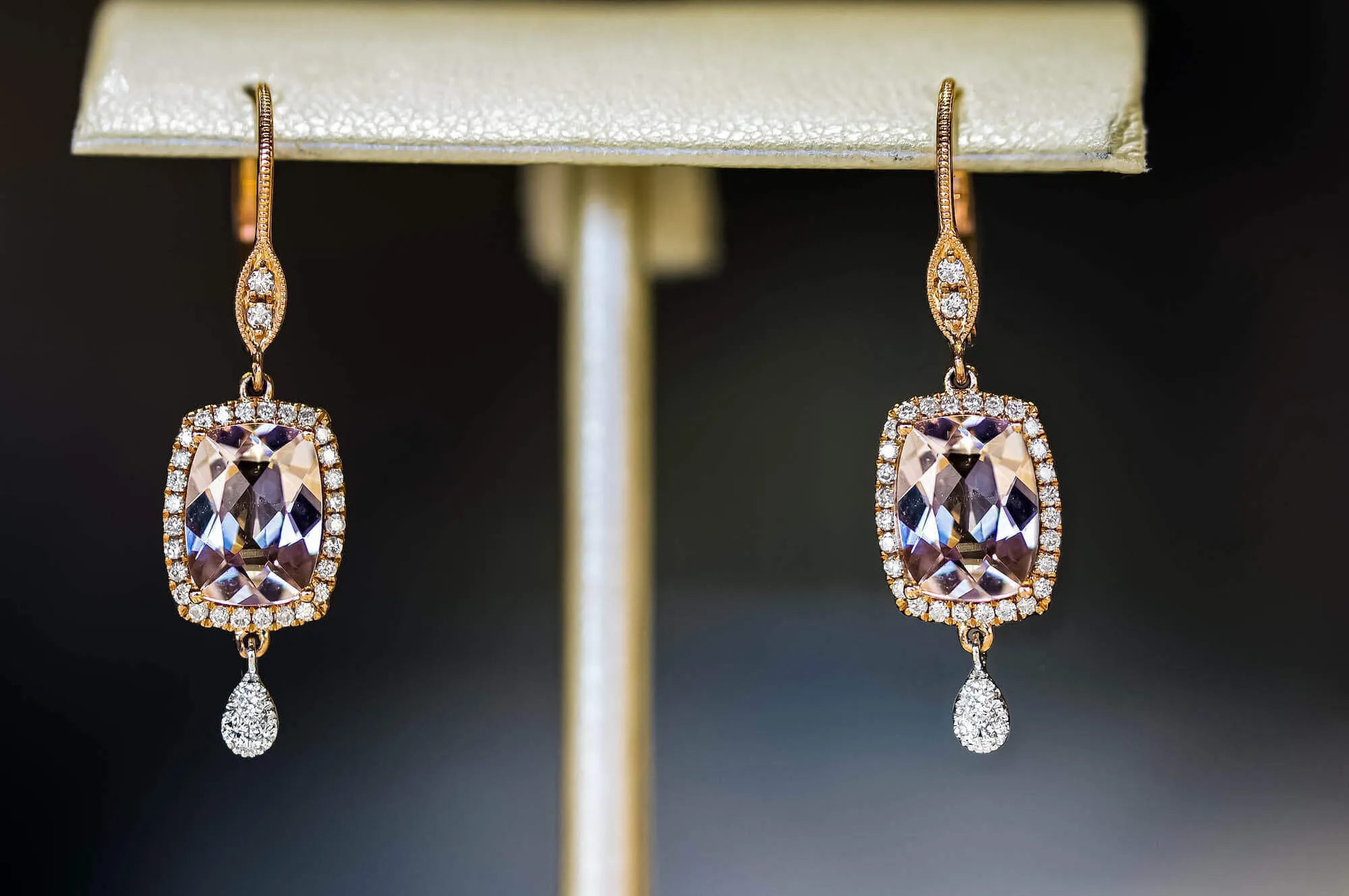 pair of light purple rectangular gemstones set in a pair of earrings. gemstone is surrounding with diamonds, and the top and bottom of each earring have an additional diamond 
