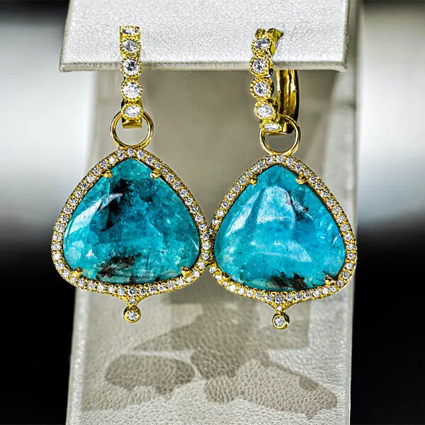 pair of teal tear drop shaped gemstones placed within a set of gold earrings