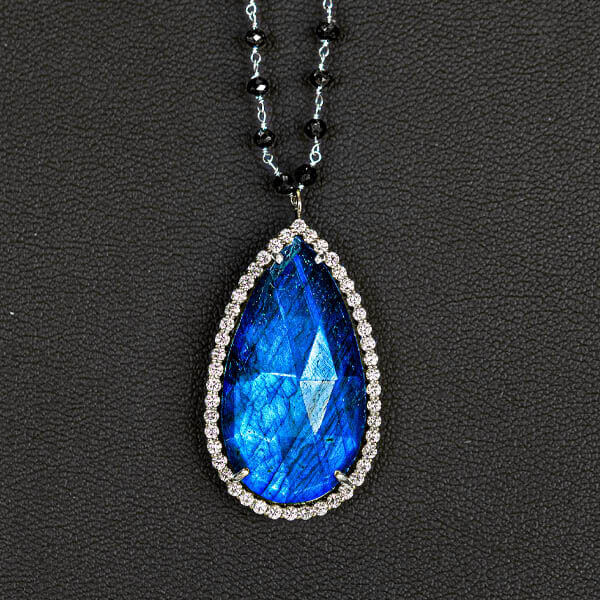 a blue gemstone in a teardrop shape placed within a gold rimmed pendant necklace