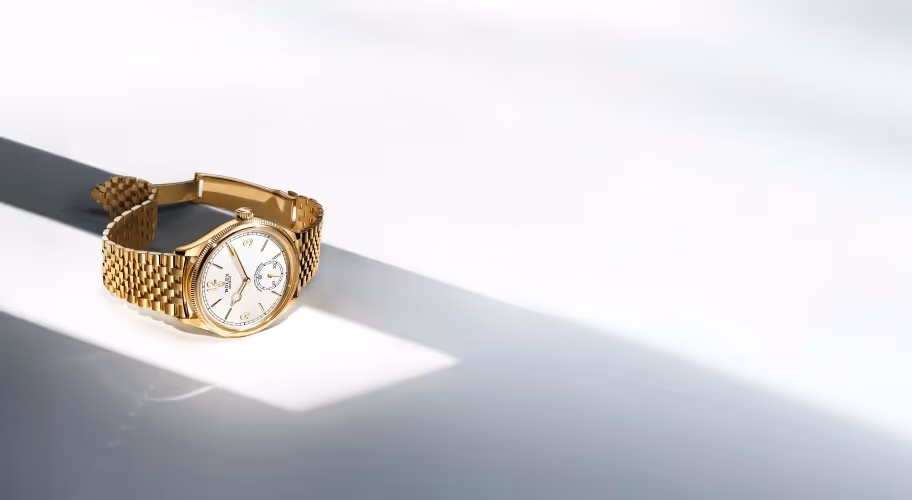 Positioned to the left against a luminous backdrop of soft gradients and shadow, the Rolex Perpetual 1908 in 18 ct yellow gold features a 39 mm case, elegant white dial, and finely fluted bezel. Its transparent case back reveals the calibre 7140, a self-winding mechanical movement with a Syloxi hairspring. Paired with a polished yellow gold Jubilee bracelet, this timepiece embodies refinement and modern precision. Jack Lewis Jewelers of Bloomington, Illinois, now at 3011 Galena Rd, is proud to be part of the worldwide network of Official Rolex Jewelers.