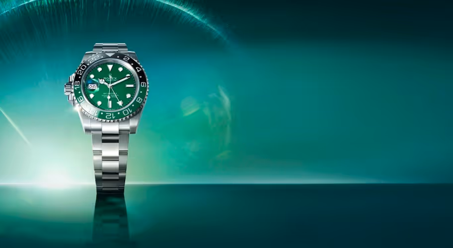 Positioned to the left against a radiant green gradient backdrop, the Rolex GMT-Master II in Oystersteel features a striking green dial and black Cerachrom bezel insert. Its robust 40 mm Oyster case, equipped with a bidirectional rotatable bezel and 24-hour graduated scale, embodies functionality and timeless design. Powered by the calibre 3285, a self-winding mechanical movement, this watch offers precision and dual time zone capability. Presented on an Oyster bracelet, the GMT-Master II is the traveler’s ultimate companion. Jack Lewis Jewelers of Bloomington, Illinois, now at 3011 Galena Rd, is proud to be part of the worldwide network of Official Rolex Jewelers.