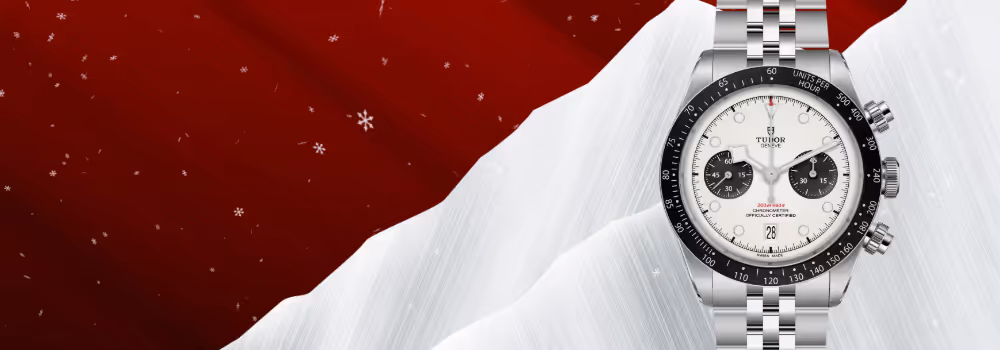 The TUDOR Black Bay Chrono, model M79360N-0014, features a 41mm stainless steel case with polished and satin finishes, a domed opaline dial with contrasting black subcounters, and a fixed tachymeter bezel in black anodized aluminum. Equipped with the Manufacture Calibre MT5813, this chronograph offers a 70-hour power reserve and COSC-certified precision. Displayed on the right side of the image against a festive red-and-silver background with softly falling snowflakes, the watch is presented on a riveted stainless steel bracelet. Jack Lewis Jewelers, located at 3011 Galena Rd, Bloomington, Illinois, is proud to be part of the worldwide network of Official TUDOR Jewelers, authorized to sell and service TUDOR watches.