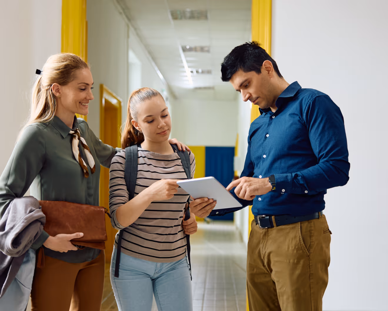 Teacher discussing tablet content with a student and parent in a school hallway