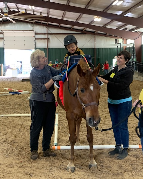 Participant riding a therapy horse with two side walkers.
