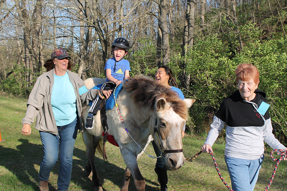 An Equine-Assisted Therapy participant riding a therapy horse with two side walkers and a leader assisting.