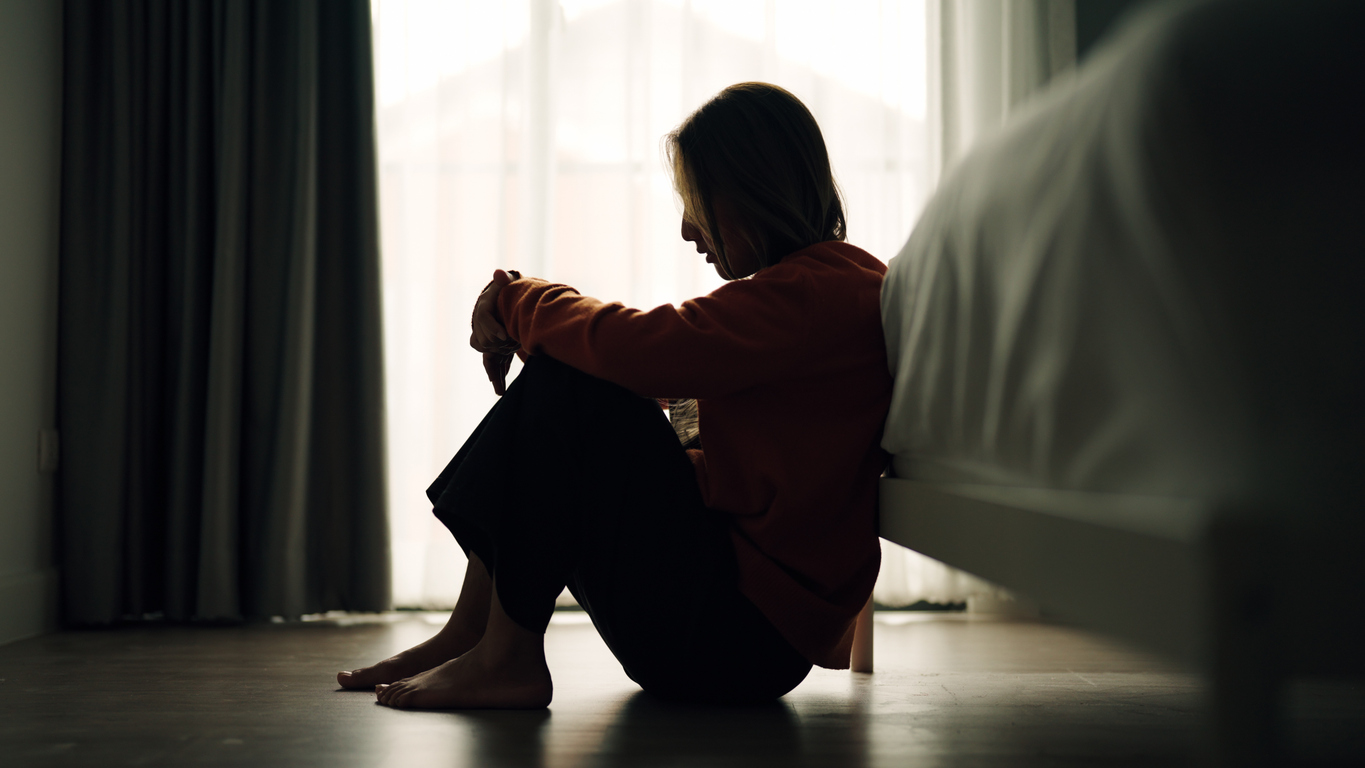 Person seated on the floor in a dark bedroom