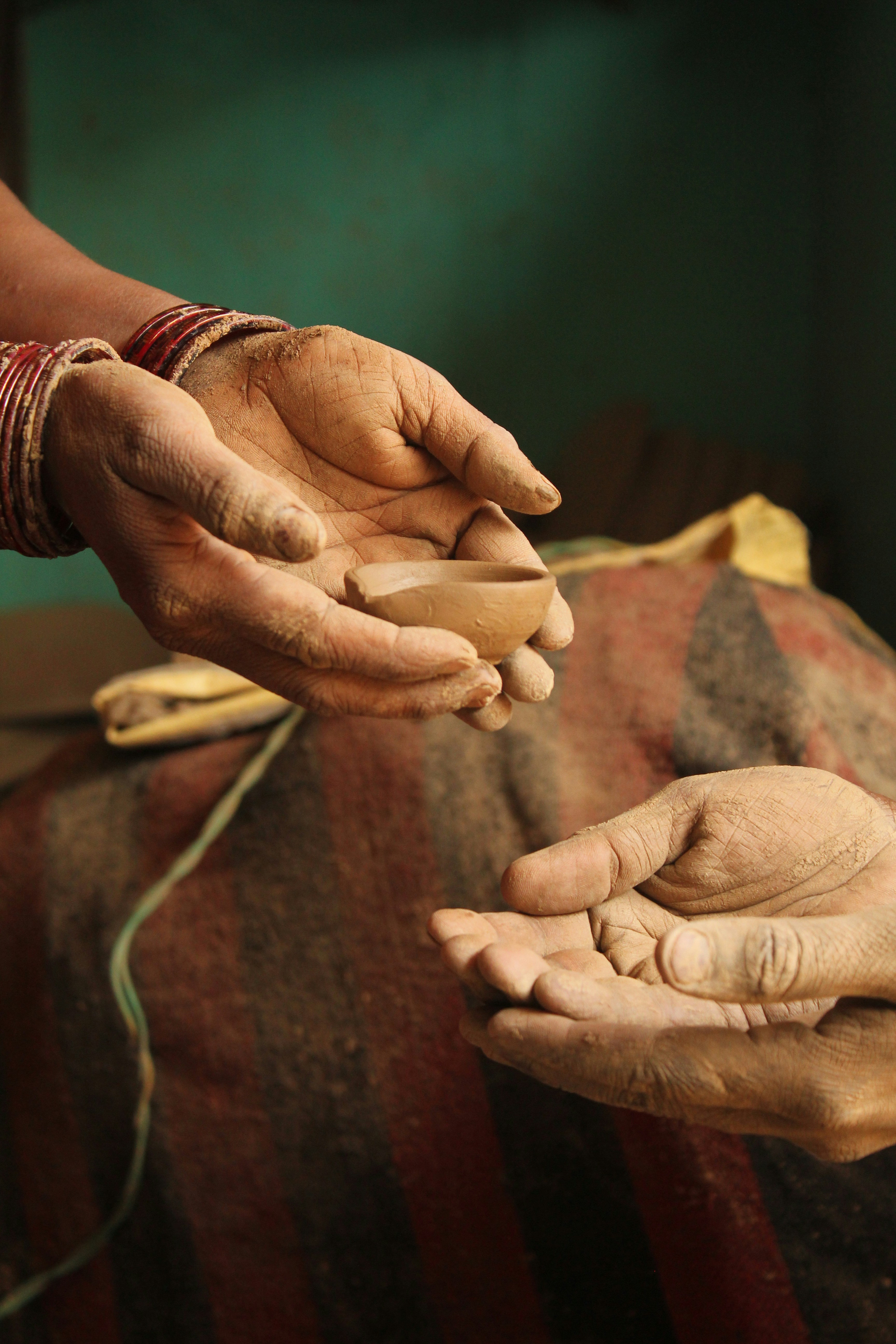 Two hands giving a small pottery piece to two other outstretched hands