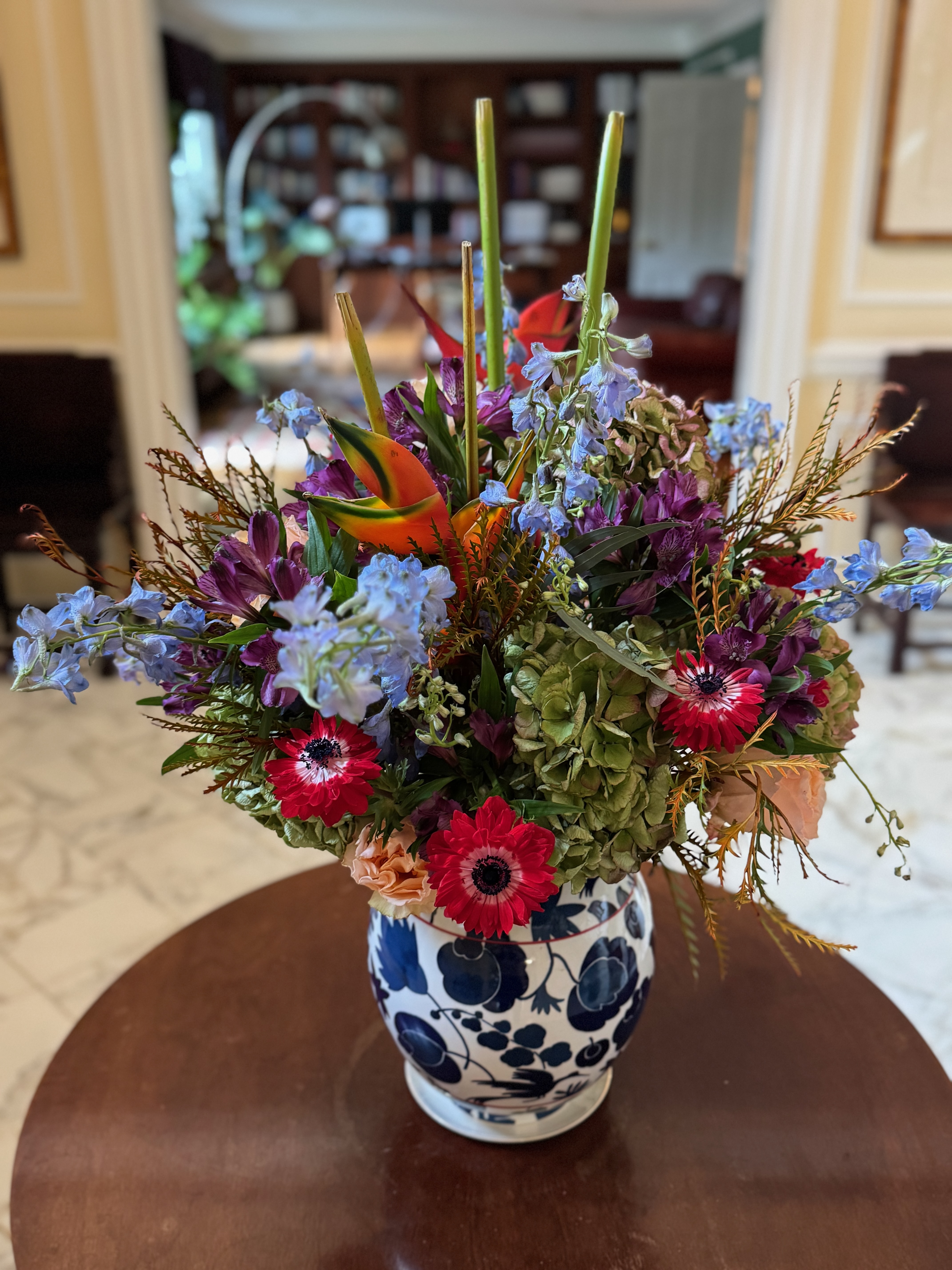 A blue, red, and purple bouquet in a white vase on a table.