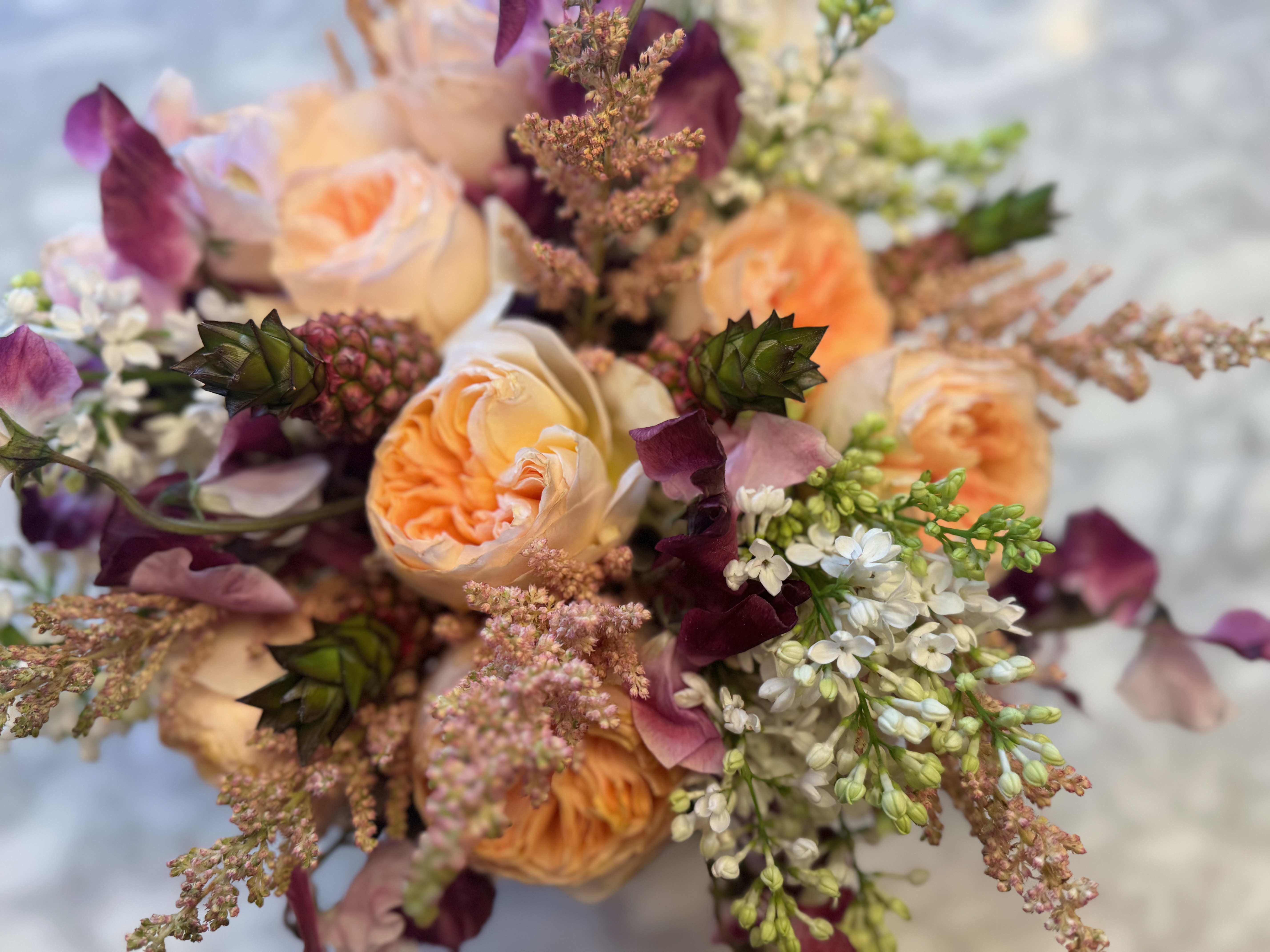 A close-up photo of a bouquet with peach roses, white baby's breath, and other purple filling flowers.