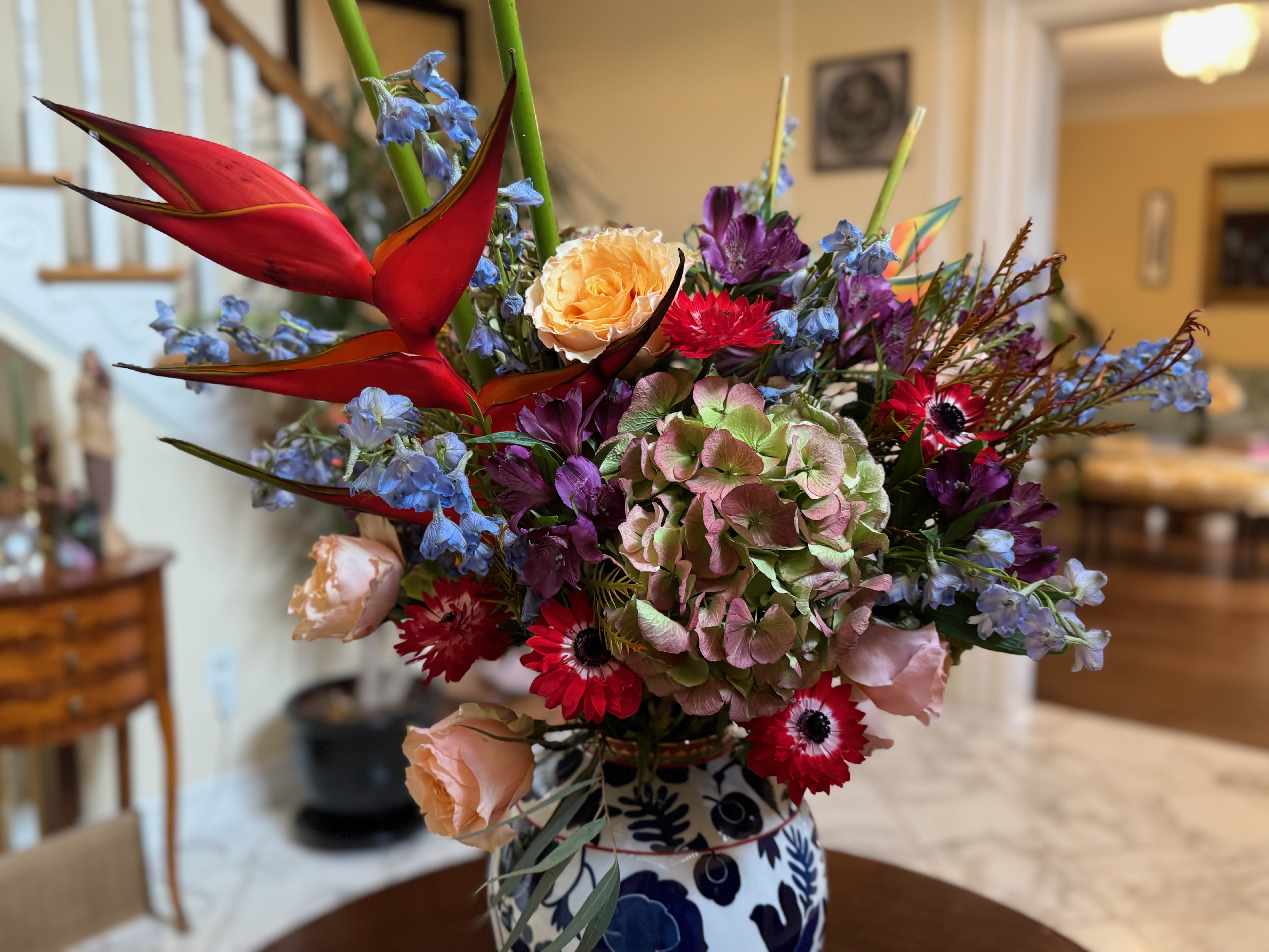 A blue, red, and purple bouquet in a white vase on a table.