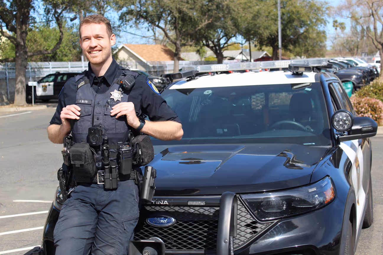 Male officer smiling in front of the police car