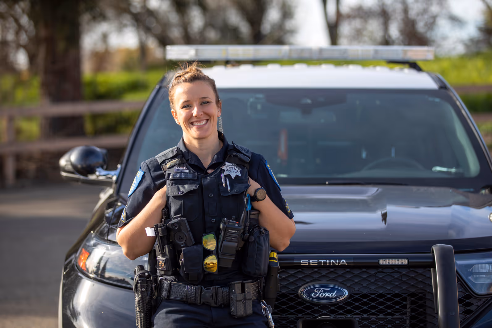 female officer smiling while standing in front of police car