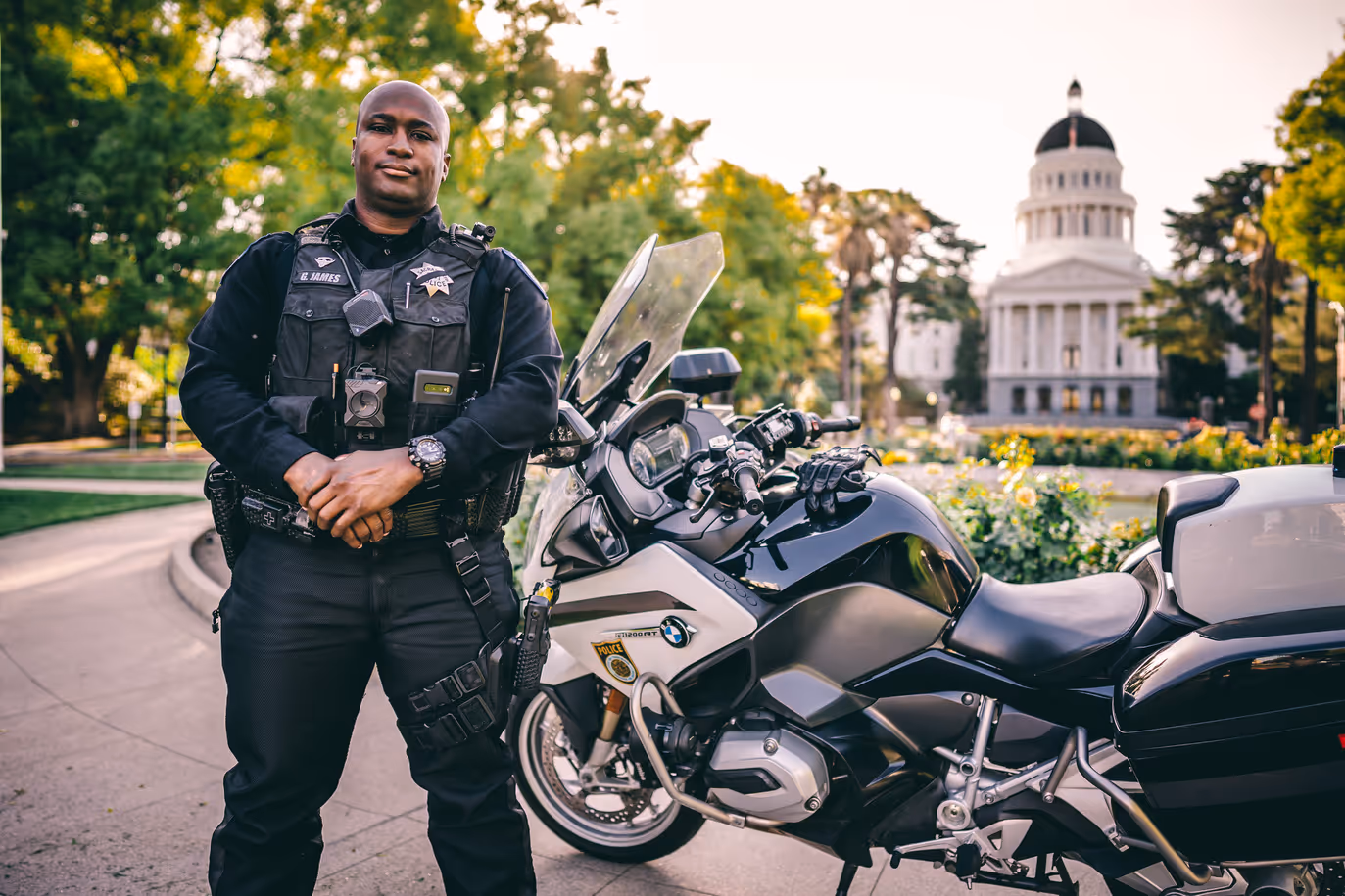 male officer standing next to motorcycle in front of the building