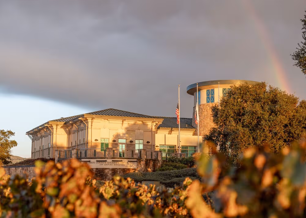 Napa County Sheriff's Office building with a rainbow in the cloudy sky and autumn foliage in the foreground.