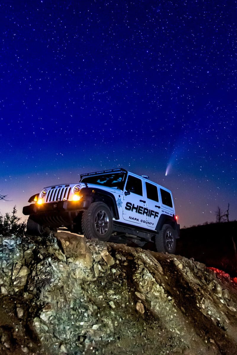 Napa County sheriff's off-road vehicle with headlights on parked atop a rocky hill under a starry night sky with a visible comet.