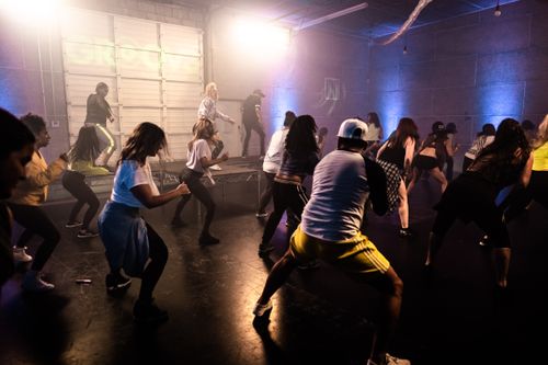 Three instructors on a stage lead a group of students in a dance fitness class.