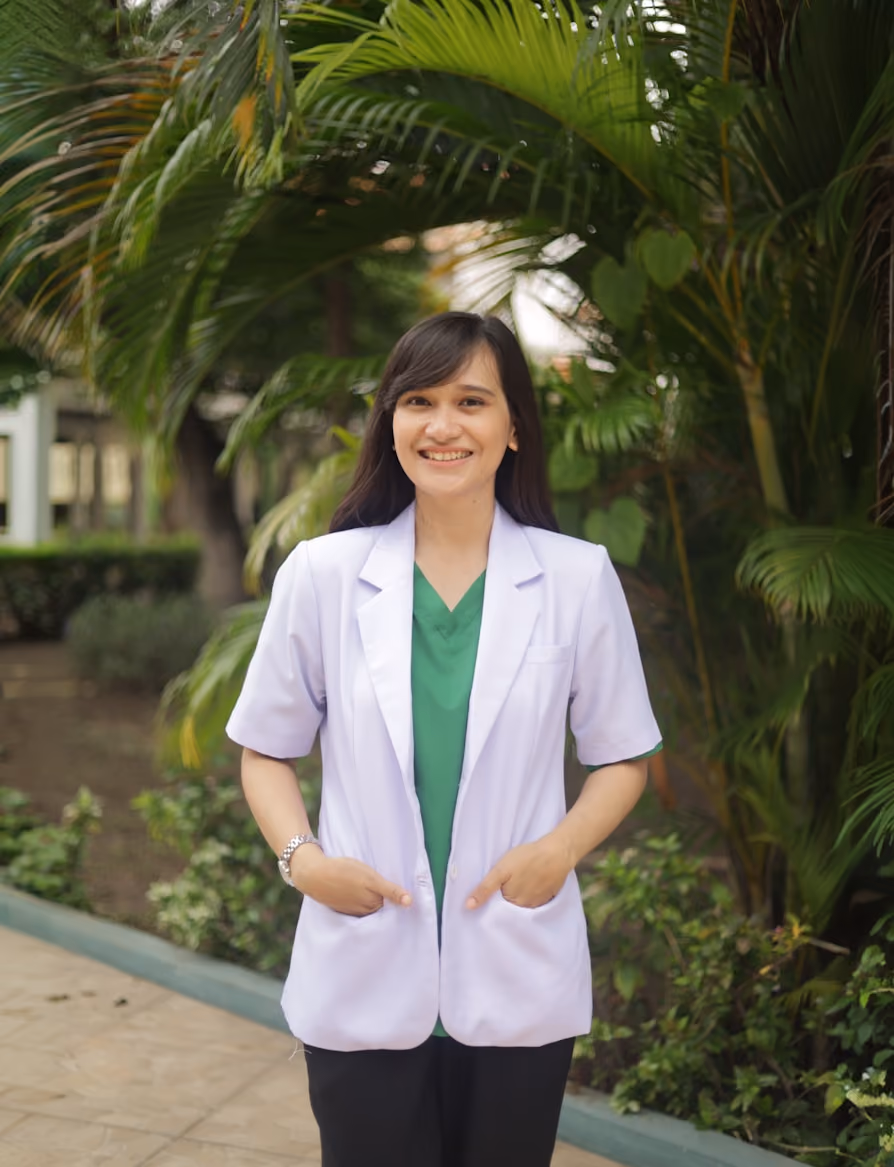 Smiling female healthcare professional in white coat standing outdoors.