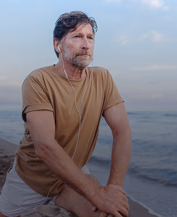 Middle-aged man stretching on the beach while listening to music.