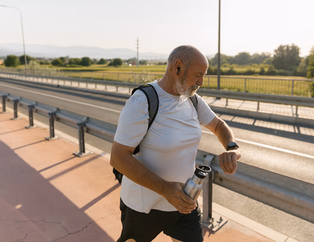 Senior man walking outdoors checking smartwatch during morning exercise.