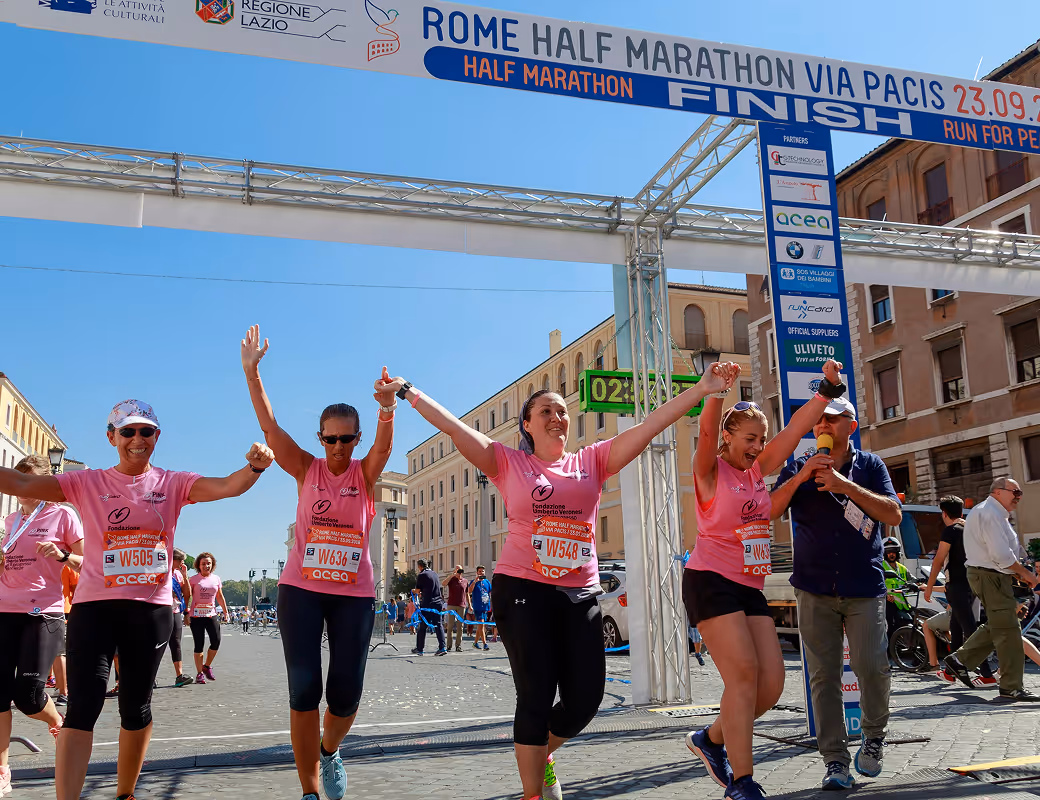 Group of women in pink shirts celebrating as they cross the Rome Half Marathon finish line.