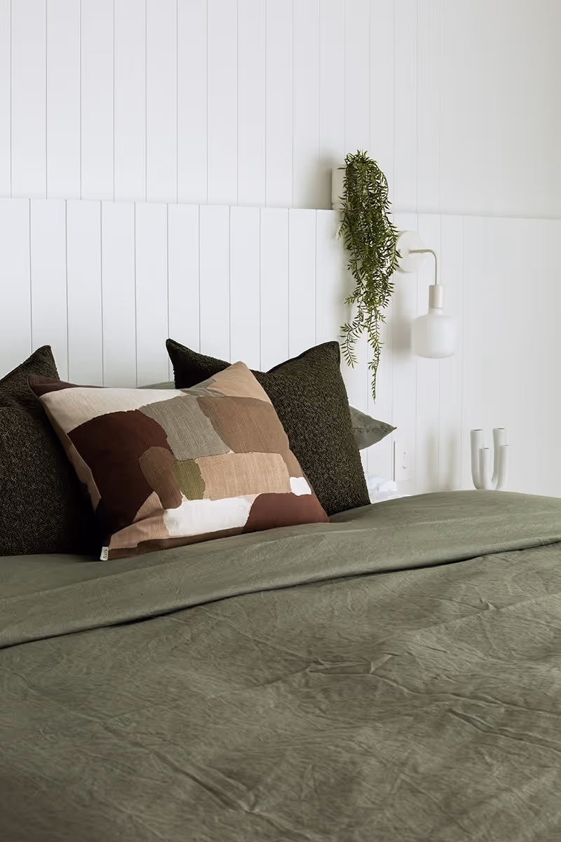 Bed with pillows and white wall with plant.