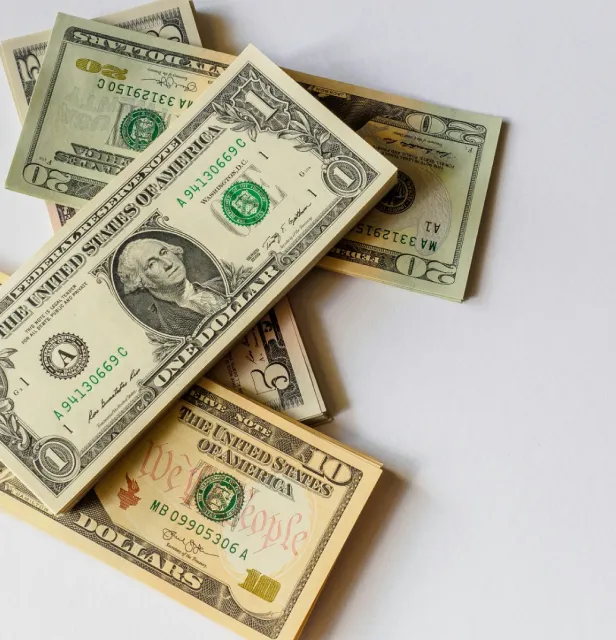 A stack of U.S. dollar bills including a one and a twenty, laid on a white surface.