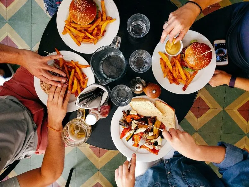4 plates with food, people's hands grabbing food.