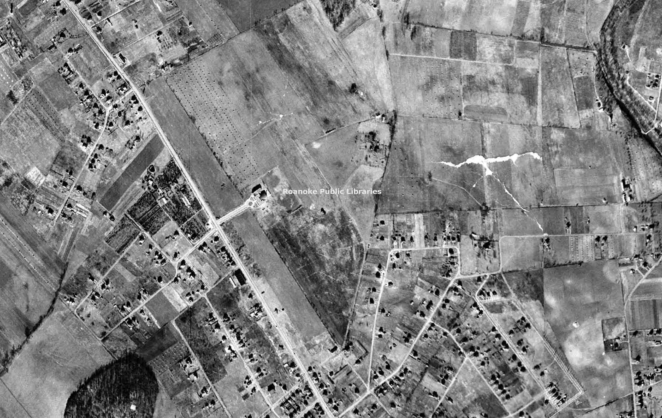 Black and white aerial photo showing farmland with scattered houses and a main road running diagonally.