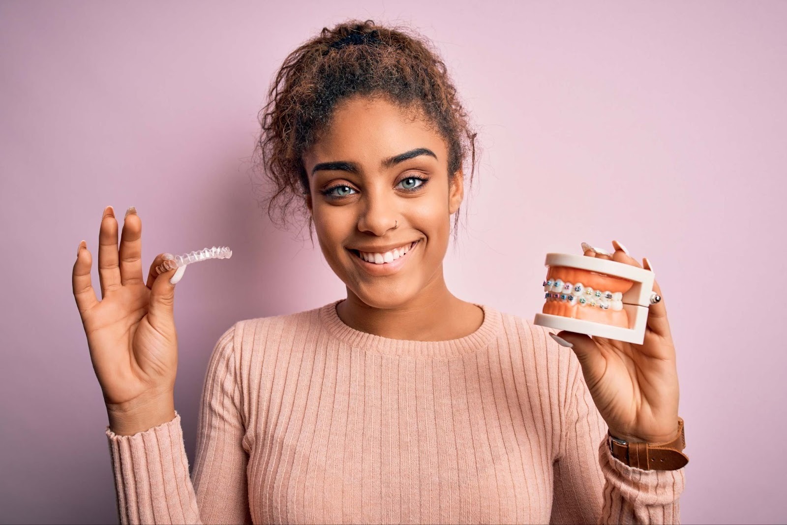 Woman holding a clear orthodontic aligner and dental model showing braces behind the teeth as discreet teeth straightening options in Upminster