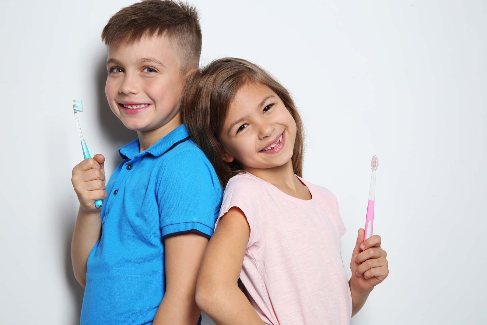 Children holding toothbrushes and smiling, promoting good oral hygiene and regular dental check-ups for families