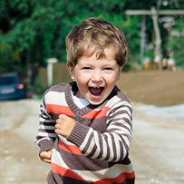 A young boy wearing a brown and white striped sweater is smiling.