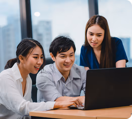 Team collaboration in a modern office setting, with three young professionals working together on a laptop. The coworking environment features large windows and a city skyline, highlighting office productivity and teamwork.
