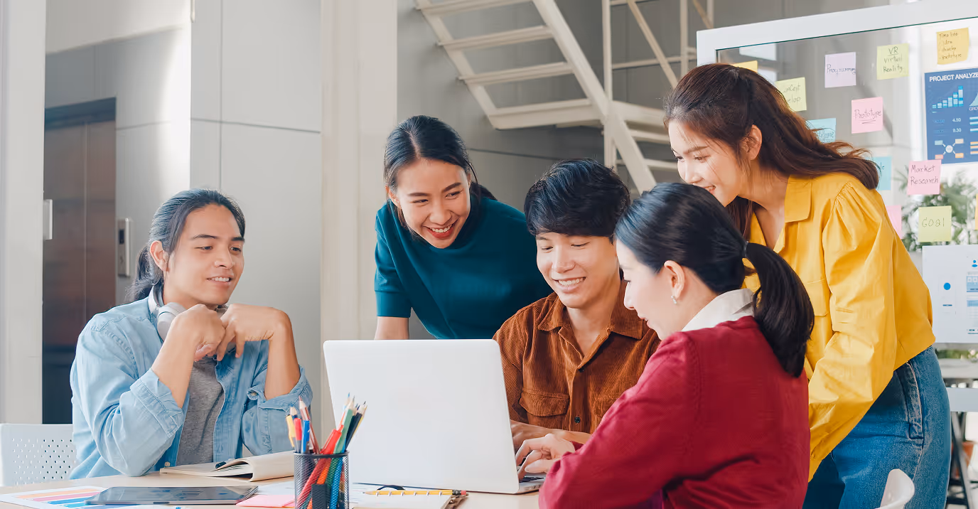 Young creative team collaborating on a laptop in a modern office, surrounded by colorful sticky notes and project planning charts. The group is brainstorming ideas for innovation, startup growth, or product development in a vibrant and casual work environment.