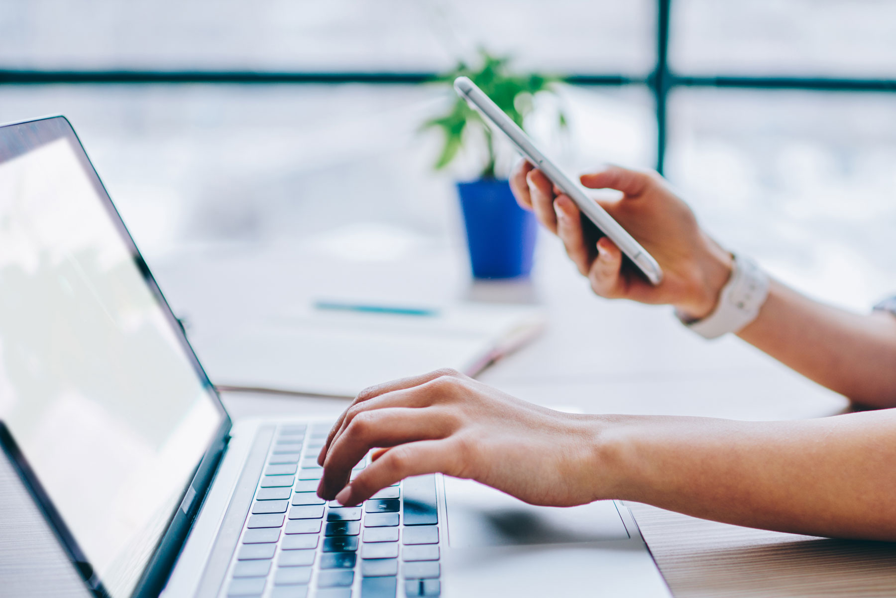 A woman typing on computer and using phone 