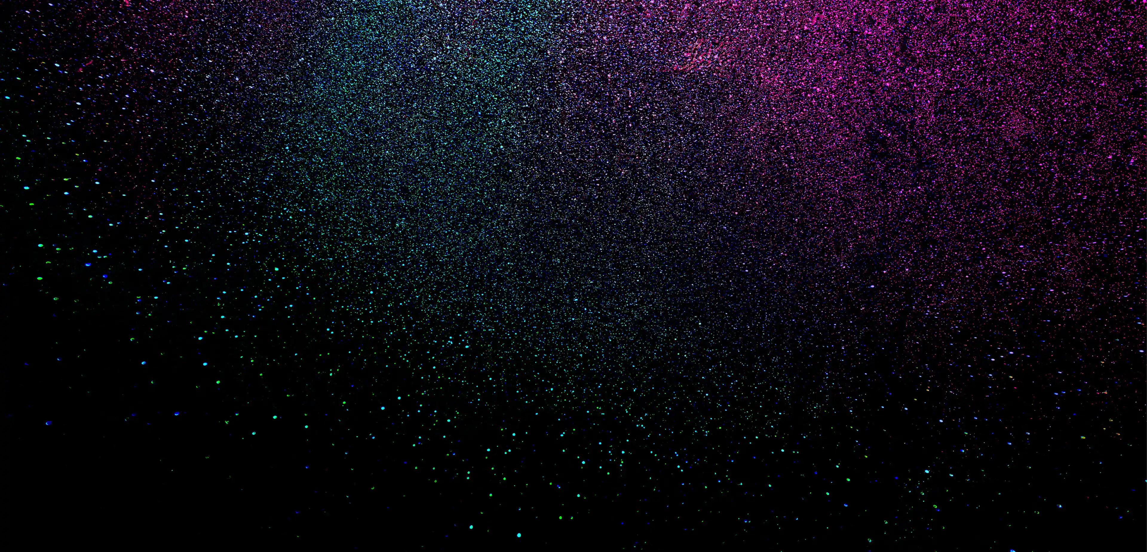 Spray of fine particles in blue, green, and pink on a black background.